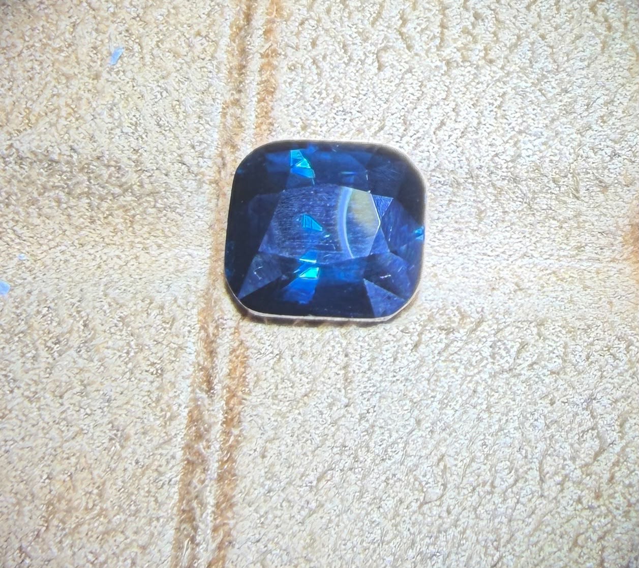 Deep blue cushion-cut gemstone on a textured surface.